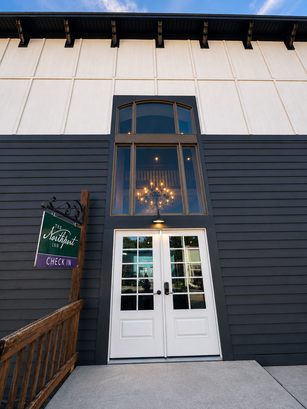 A hotel entrance with a sign, double doors, and a large window above the doors.